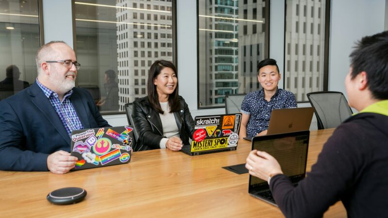 Meeting of people with laptops covered in stickers in a highrise boardroom