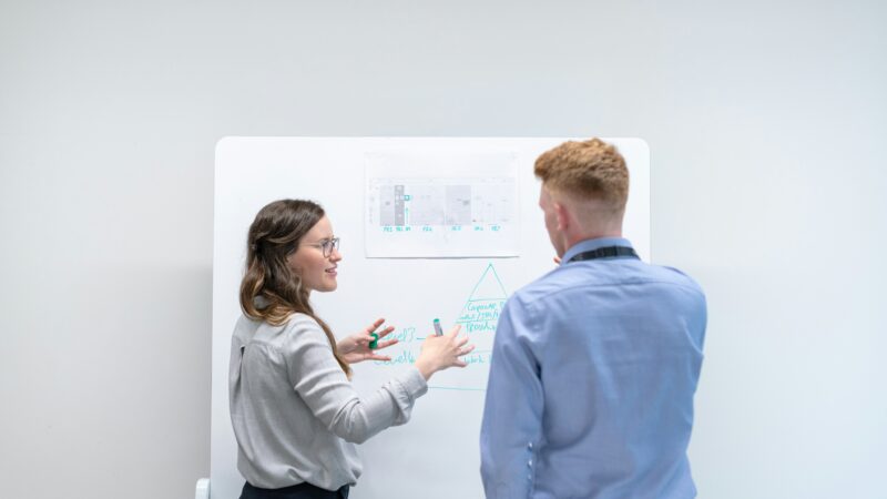 Woman explaining process to man using whiteboard